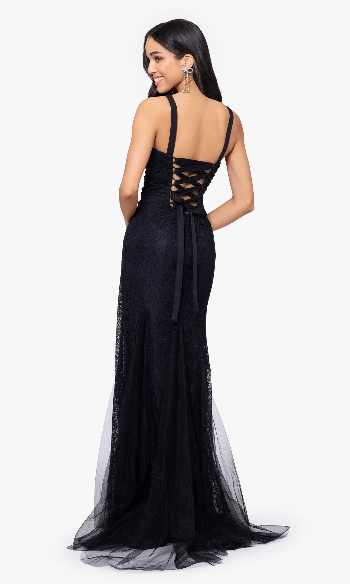 A woman stands smiling over her shoulder, wearing the Long Prom Dress 4591BN by Blondie Nites—a black lace fitted gown with a lace-up back.